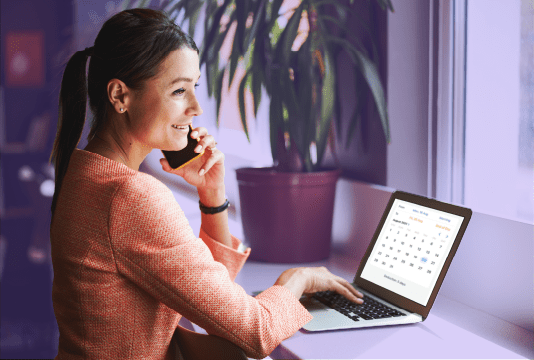 An employee is smiling while using vacation management software on their laptop to book time off.