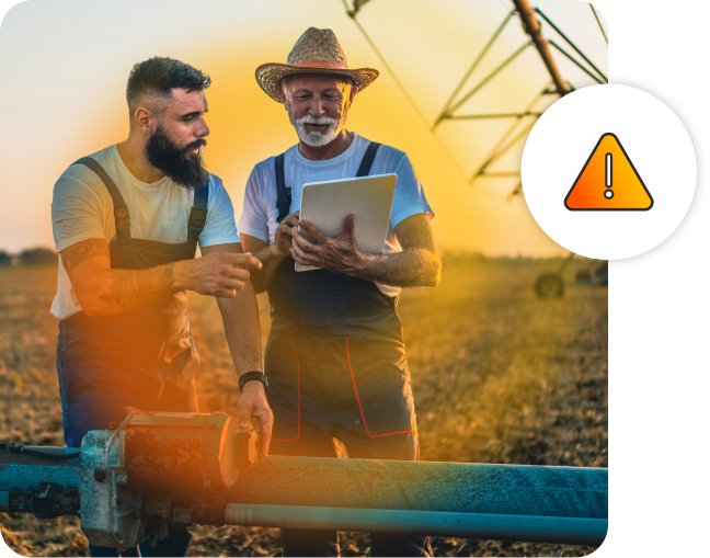 Two male farmers looking at a digital tablet while standing in a farm field with farming machinery.