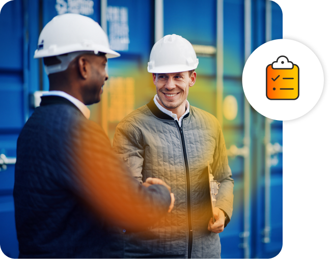 Two men shaking hands in front of a shipping container, both smiling. The one man is holding a clipboard.