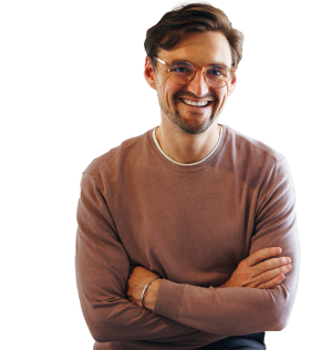 Man smiling at camera with his arms crossed, wearing a beige sweater.