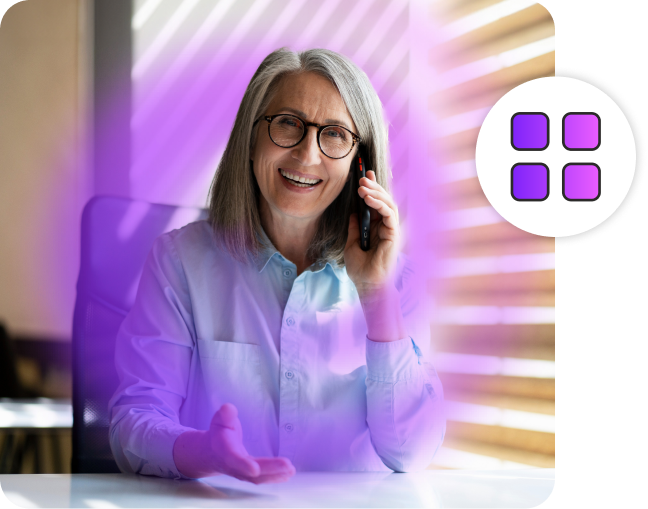 Woman smiling while having a conversation on a phone in an office.