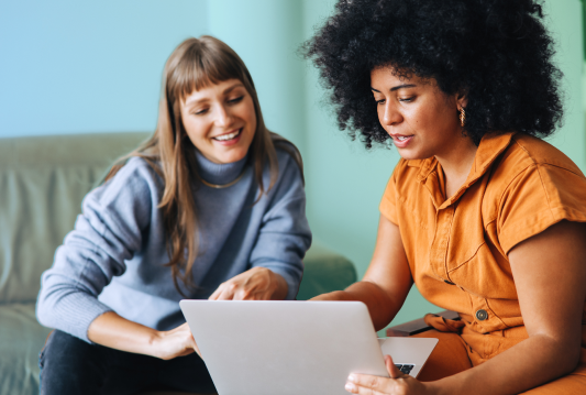 Workplace wellness in the office is being discussed by to smiling employees looking at a laptop.