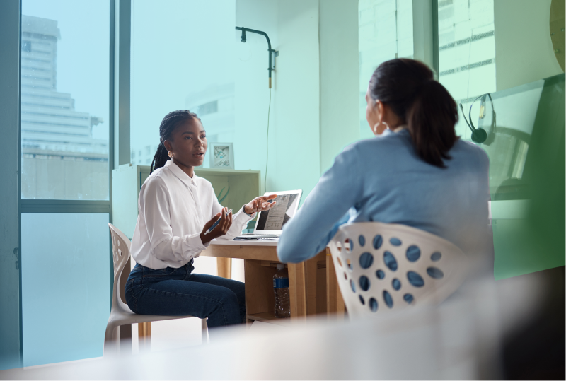 One employee is confiding in another employee while they are seated at their desks